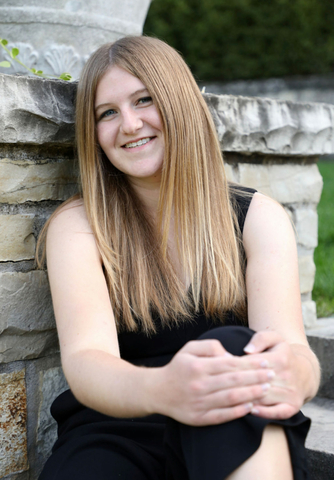 Corinna Thomas seated in front of a stone brick wall, wearing a black dress.