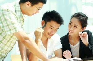 three people at a table together talking over a book