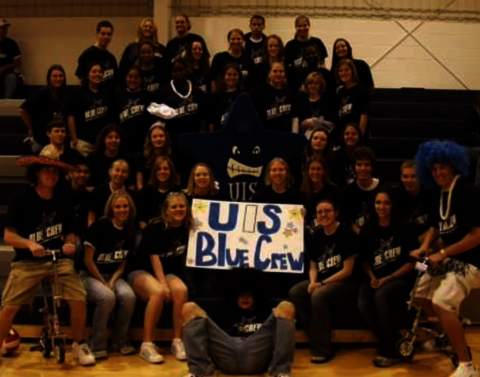 Students gathered around a sign that says "UIS Blue Crew" in a gym.