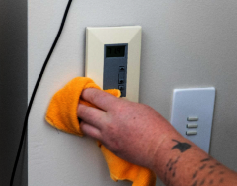 hand with a cloth cleaning a thermostat.