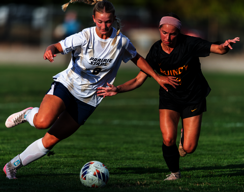 UIS woman soccer player kicking a soccer ball while holding off a defender.