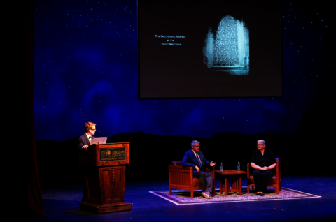 Center for Lincoln Studies Director Jacob Friefeld stands at a podium on a stage, Christopher Oakley and Michelle Krowl are seated at center stage.