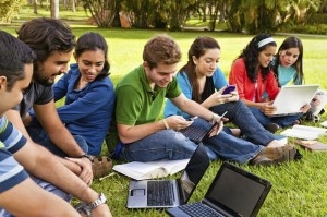 students sitting on grass doing their homework on laptops while socializing