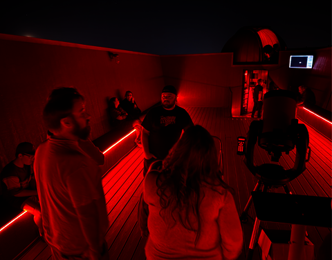 A group gazes at the sky in a red room with no roof.