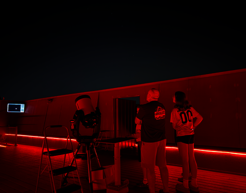 A group gazes at the sky in a red room with no roof.