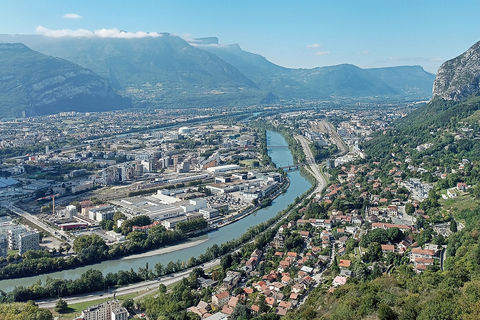 Mountain-top view of Grenoble, green trees, bright blue river flowing with orange roof houses and large Alpes mountains nearby
