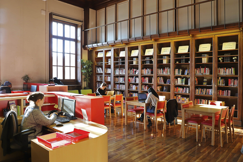 University building with red accents and students studying at desks with books on shelves behind them