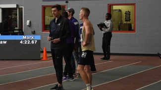 Emmons King in dark blue UIS windbreaker stands with UIS runners inside a track facility.