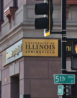 A building with a sign reading University of Illinois Springfield and a traffic light.