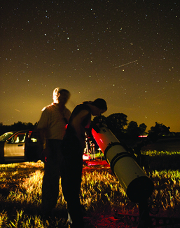 Two people using a telescope to stargaze in a field at night under a star-filled sky.