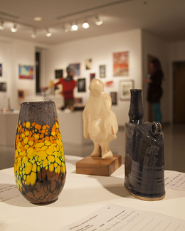 Art gallery with colorful vase, sculpture, and dark vase on display.