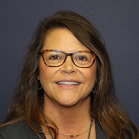 Pam Francis, a woman with glasses, smiling against a dark background.