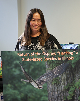 A woman standing, holding a large poster of an osprey in flight.