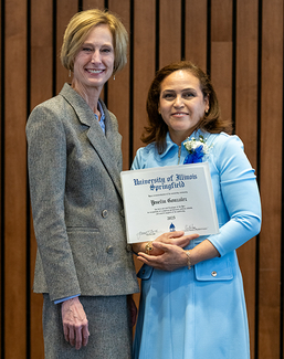 Two women smiling, one holding a certificate, standing indoors.