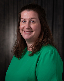 Smiling woman in a green shirt against a dark background.