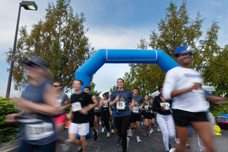 Runners starting a race under a blue inflatable arch, with trees and cloudy sky.