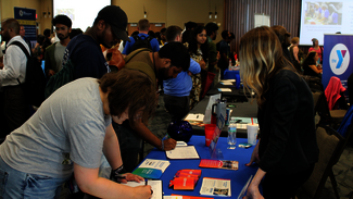 Busy career fair with people interacting at tables.