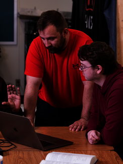 Two men discussing something on a laptop, one pointing at the screen.