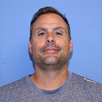 Man in a gray shirt against a blue background, looking at the camera.