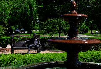 Fountain and bench with statues in a lush green park.