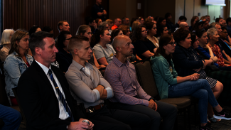 Audience attentively listening in a dimly lit conference room.