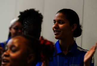 People clapping in a dimly lit room, wearing casual blue shirts.
