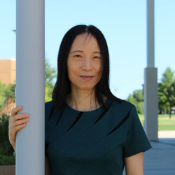 Woman stands outdoors, smiling under a clear blue sky