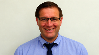 Smiling man wearing glasses, blue shirt, and navy tie.