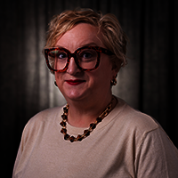 Sarah Adams smiling at the camera with a grey background.
