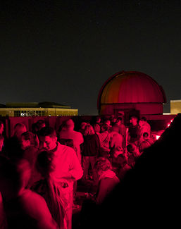 Crowd under red lighting at night, with dome in the background.