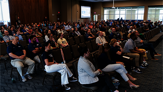 Audience seated in a large conference room, attentively watching a presentation.