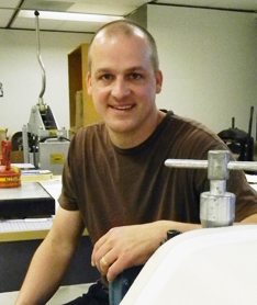 Man looking at the camera in printmaking shop surrounded by machinery.