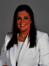 Summer Quesenberry portrait in a white blazer and white top, gold necklaces, long dark hair.