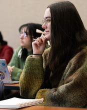 A student in class smiling with a notebook on the desk and pen in hand.