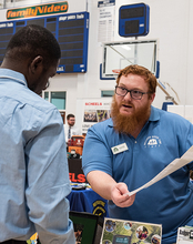 A man holds a piece of paper while talking to a student about a job.