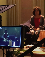 A camera and screen and shown capturing an image of a girl sitting on a couch.