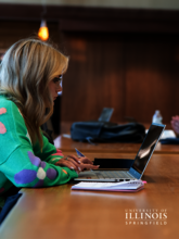A girl is sitting at a desk in the library looking at a laptop.