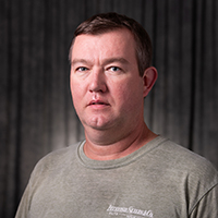 Cory Strawn, a man in a grey shirt with a neutral expression, dark background.