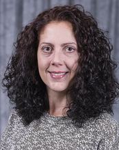 Smiling woman with curly hair against a gray backdrop.