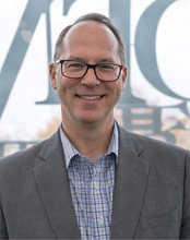 Smiling man in glasses and suit, standing indoors.