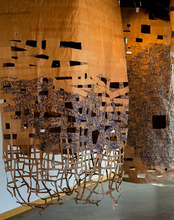 Hanging woven art installation with cutouts, warm tones, near windows.