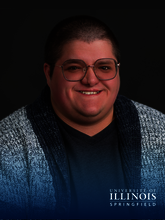 Smiling person wearing glasses and a textured cardigan, dark background.