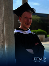 Graduate smiling in cap and gown, standing outside near a pillar.
