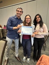 Three people smiling, one holding a certificate in a conference room.