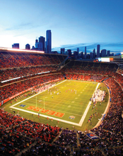 Football stadium at dusk with city skyline in background.