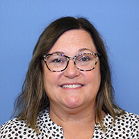Smiling woman with glasses, against a blue background.
