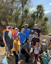 Group of people posing outdoors with trees and mountains in the background.