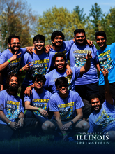 A group of smiling people in matching purple shirts outdoors.