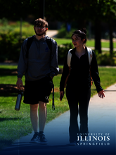 Two students walking on a sunny university campus path, smiling, with backpacks.