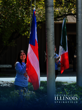Two people raise flags outdoors in front of a building.